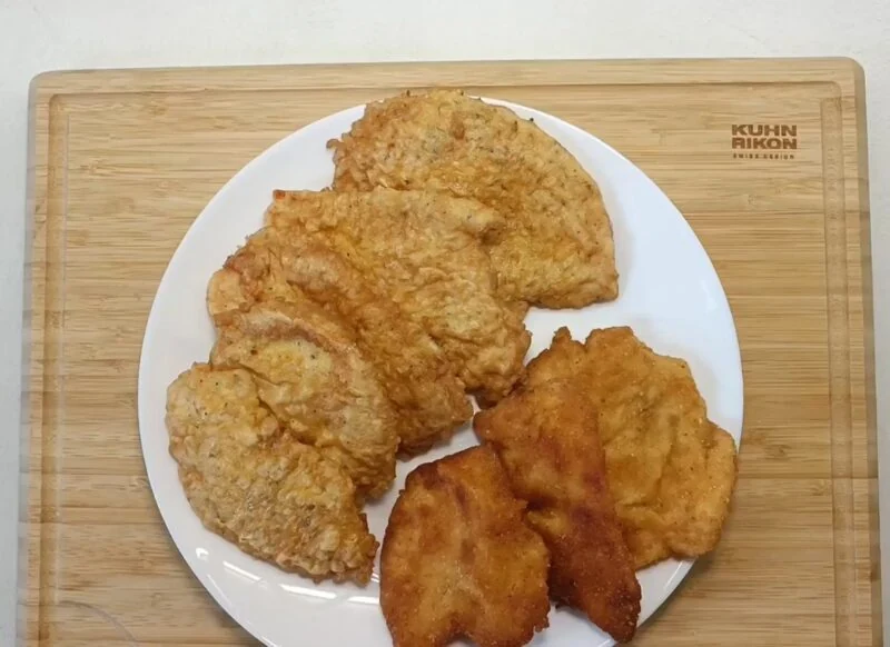 prikaz pohovane pileće snicle na belom tanjiru i drvenoj dasci