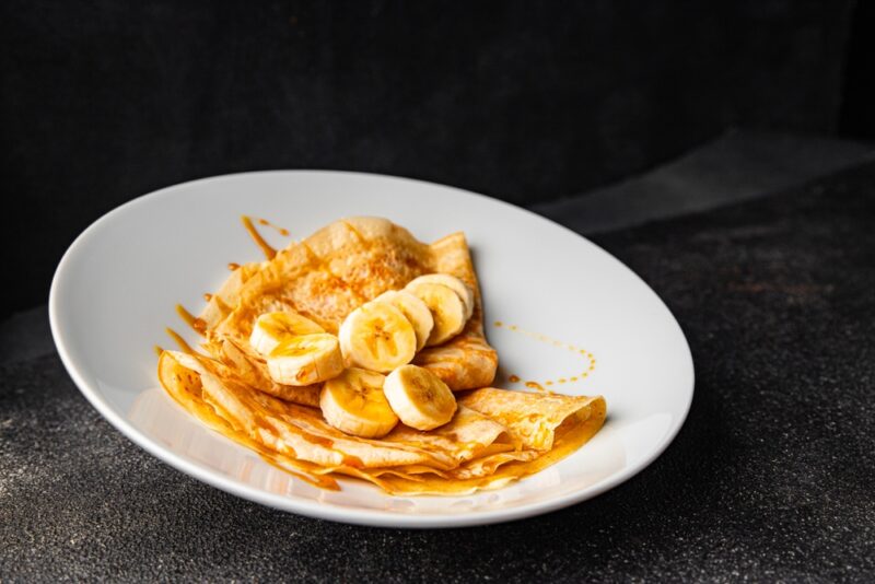 Palačinke servirane na tanjiru sa kolutovima banane i prelivom