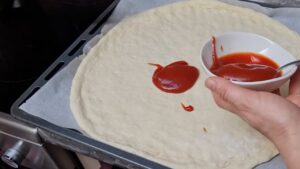 Nanošenje domaćeg sosa za picu na sveže pripremljeno testo
